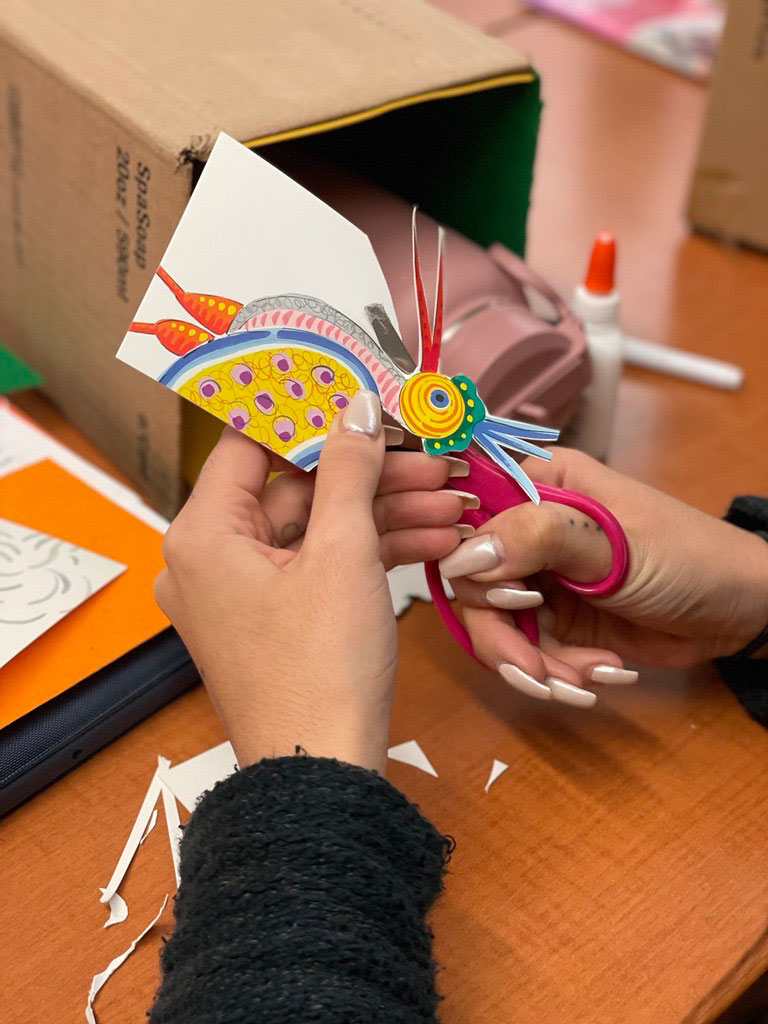Hands with scissors cutting a colorful piece of paper.